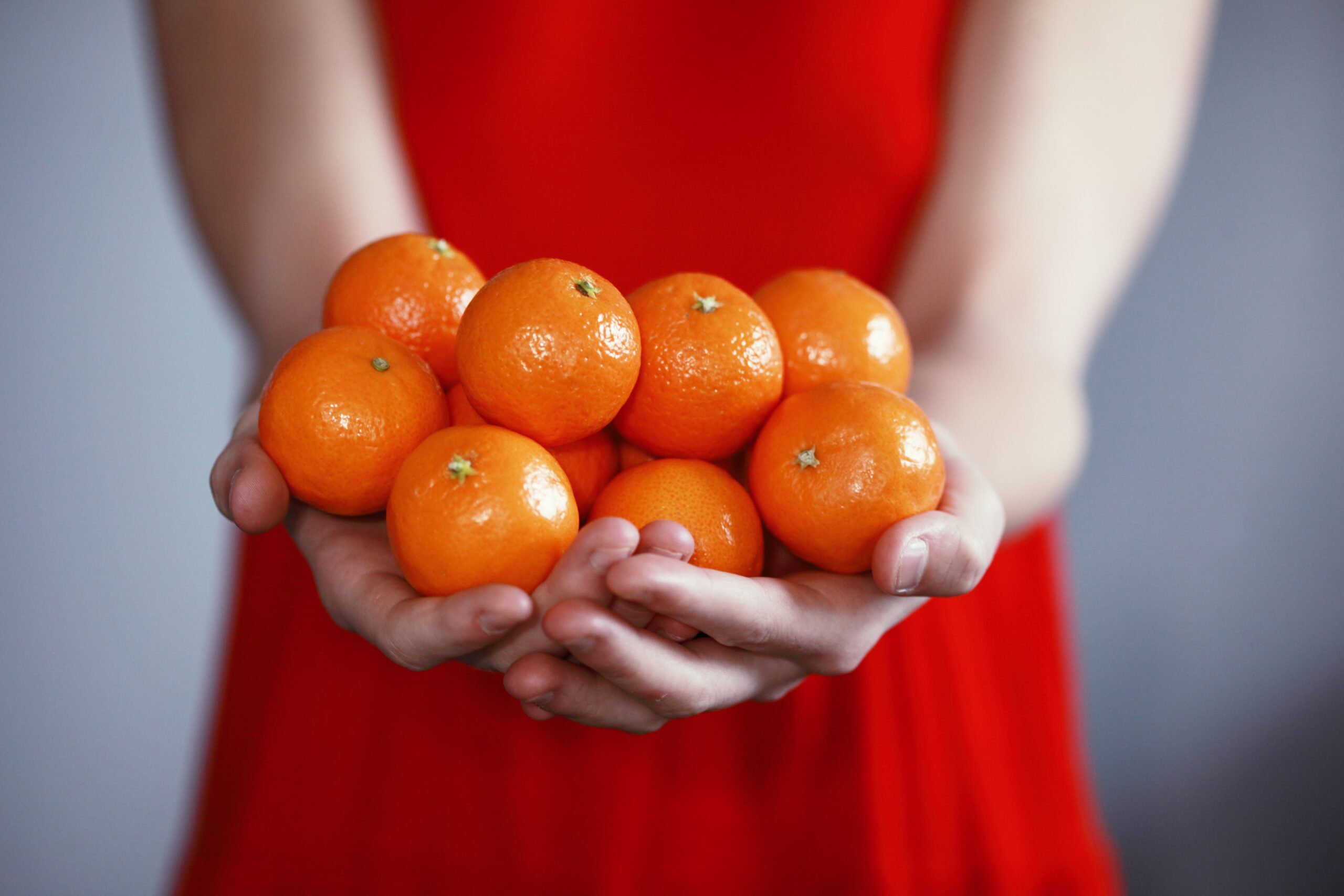 Woman in red dress holding an abundance of oranges