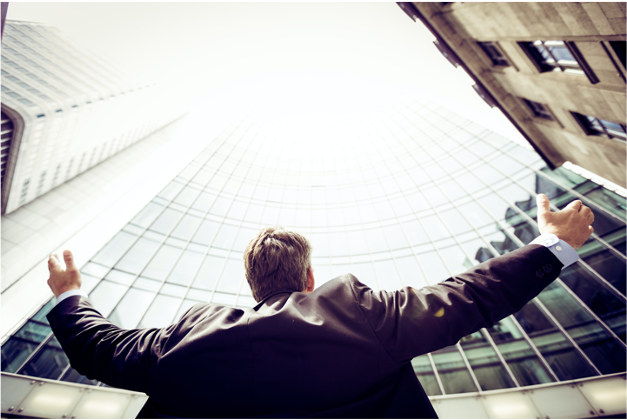 Man looking up at tall buildings with his arms raised.