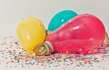 Three different sized birthday balloons laying on top of confetti.