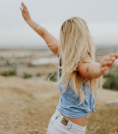 Young blonde woman in blue top with arms spread about enjoying life.
